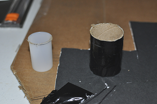 A paper towel roll, upright on table. Roll has been taped around it with black duct tape.