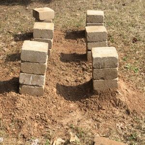 Photo of 6 columns of pavers, stacked 3 or so high. Photo shows that one column is leaning a bit, indicating that beehives would not be stable there yet.