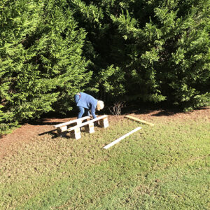 Photo of a woman in a yard, placing board onto paver stones