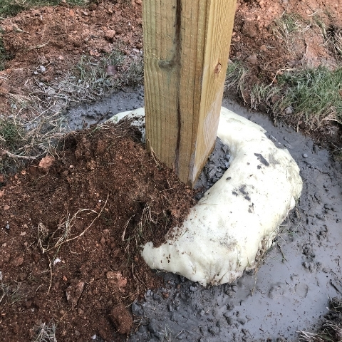 photo of wooden post in the ground with dry concrete mix poured at bottom before to setting