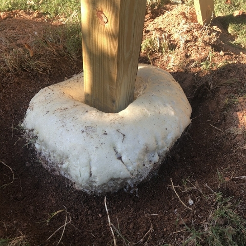 photo of a wooden post in a hole in the ground with a tan plastic looking substance around the post at  bottom