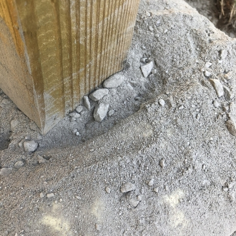 photo of wooden post in the ground with dry concrete mix poured at bottom before to setting