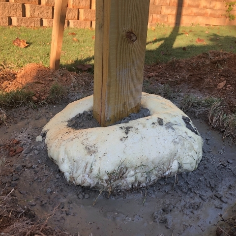 photo of wooden post in the ground with concrete mix poured at bottom waiting to setting